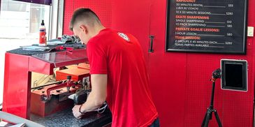 A man sharpens ice skates in a red-themed skate shop.