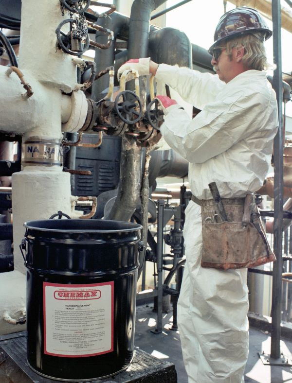 Worker in protective suit operating industrial valves near a labeled container.