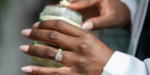 A close-up of a hand with a diamond ring holding a glass jar.
