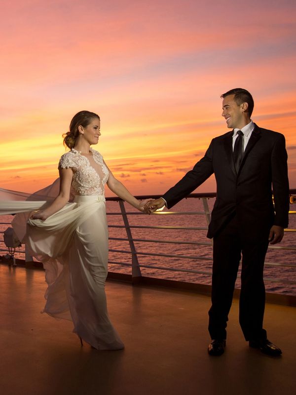 Bride and groom holding hands at sunset on a ship deck.