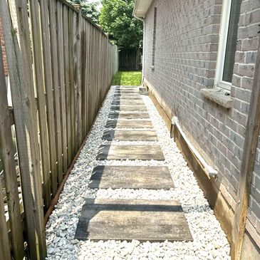A stone pathway with white gravel between a wooden fence and a brick house.