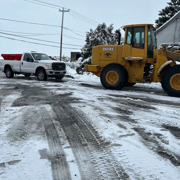 Snowy construction site with a white truck and yellow Deere loader.