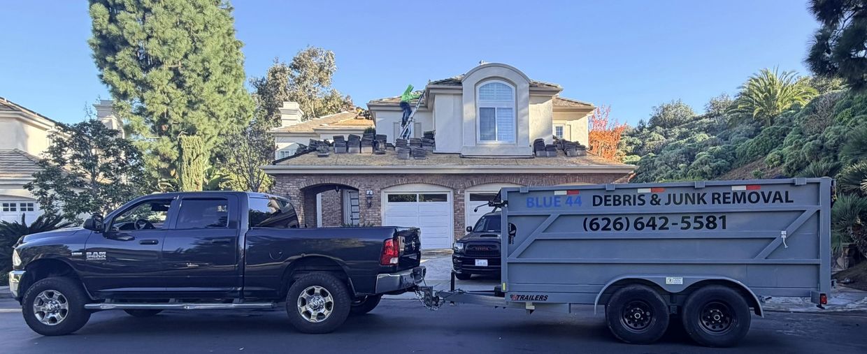 A black truck towing a trailer for debris and junk removal in front of a house roof being repaired.