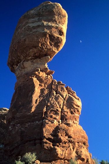 Arches National Park, Utah, Balanced Rock with moon in sky, large rock balanced atop formation.