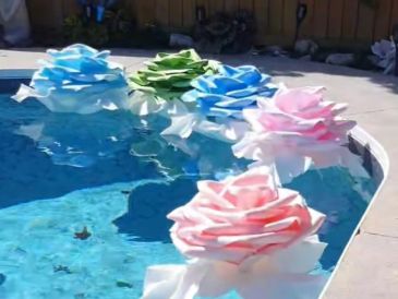 Colorful large artificial flowers floating on pool water near the edge.