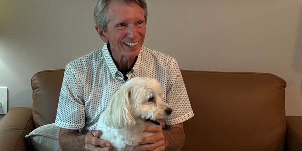 Elderly man smiling with a white dog on his lap.