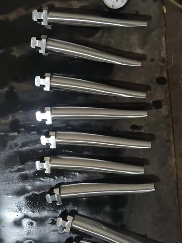 Ten metallic cylindrical parts and a round gauge on a dark surface.