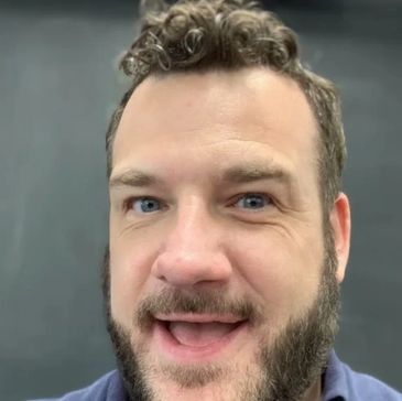 Smiling man with curly hair and beard in a blue shirt.