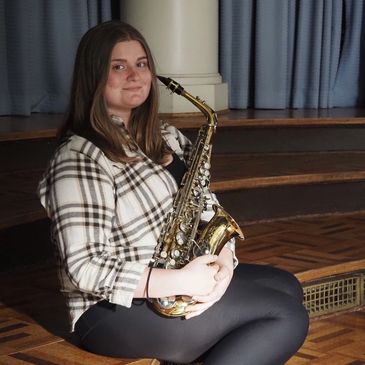 Young woman sitting with a saxophone, smiling at the camera.
