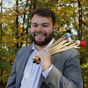 Smiling man holding percussion mallets outdoors in autumn.