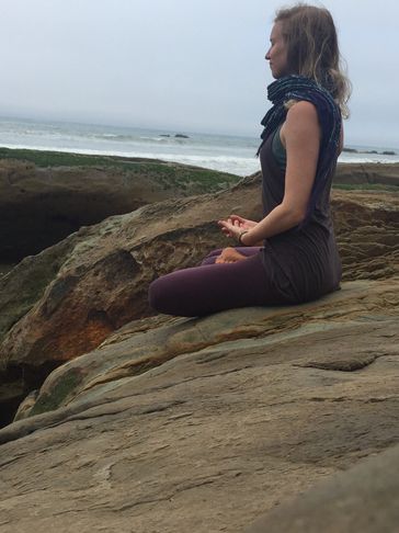 Women sitting in meditation on a rock at the beach.