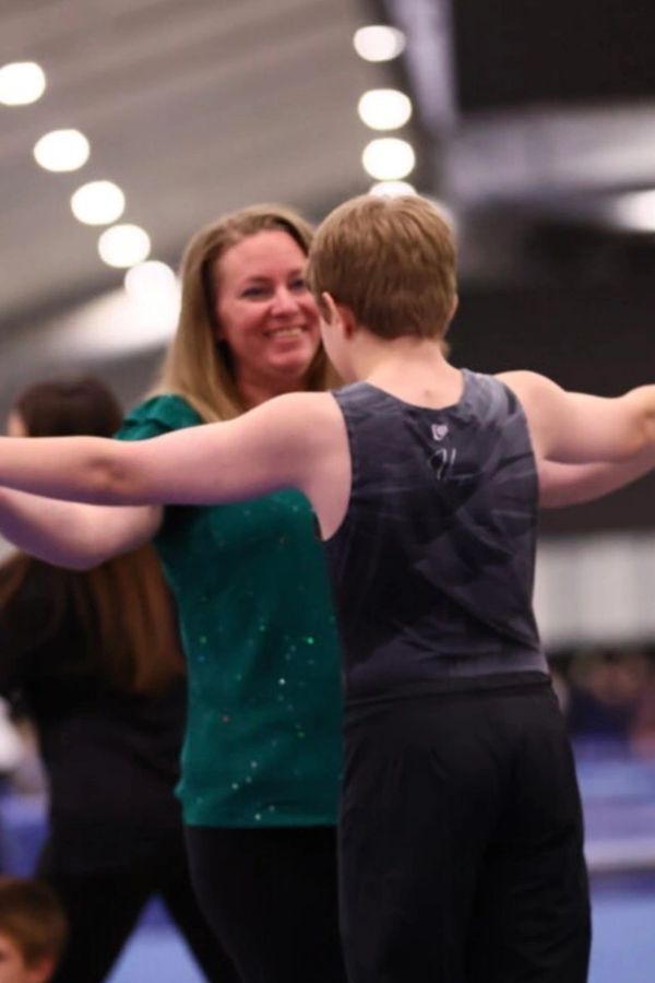 Woman coaching young gymnast with arms outstretched.