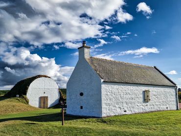 White stone cottages with a grassy mound and blue sky.
