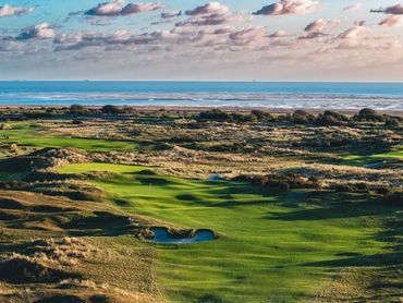 Coastal golf course with green fairways and blue ocean under a cloudy sky.