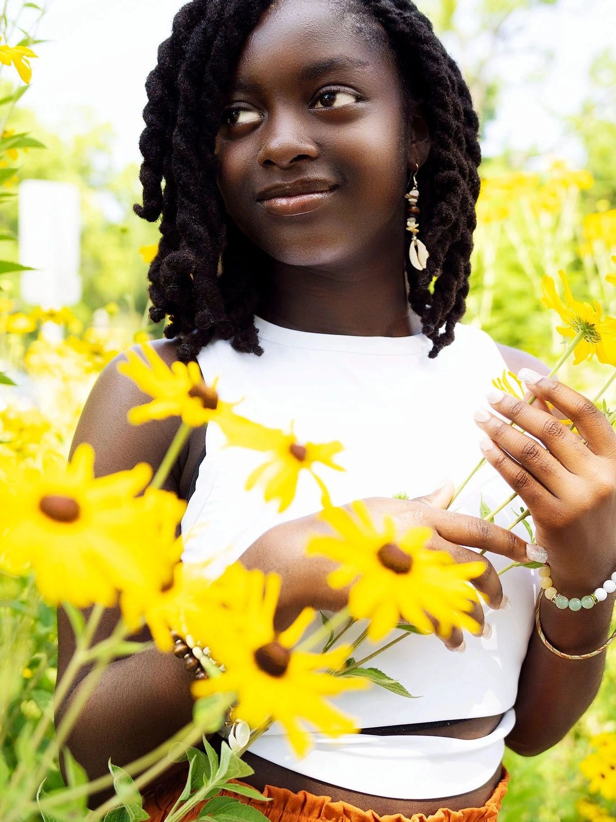 Young woman with braided hair holding yellow flowers in a sunny garden.
