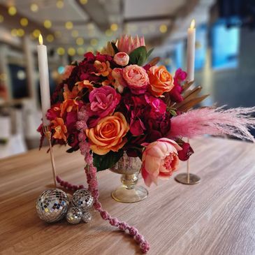 Elegant floral centerpiece with candles and disco balls on a wooden table.