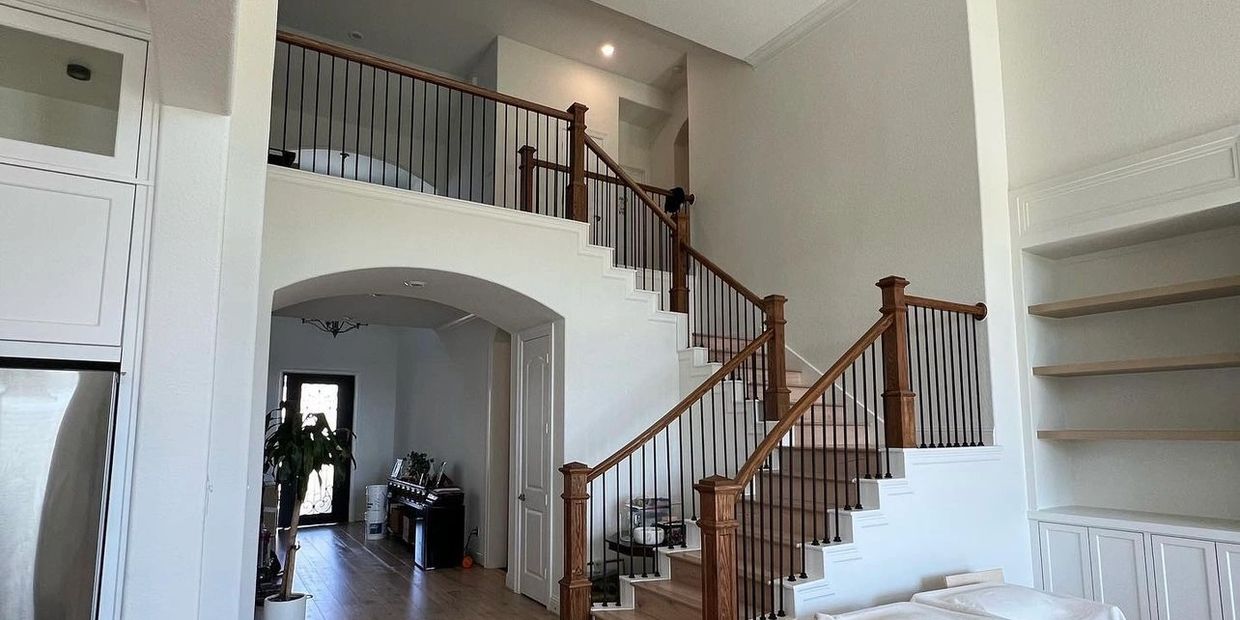 Modern staircase with wooden railing and black balusters in a bright home interior.