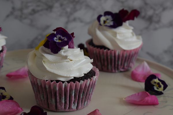 Two cupcakes with white chocolate icing topped with an edible flower