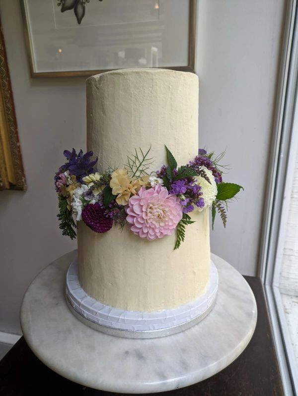 A two tier cake decorated with a purple flower arrangement. 