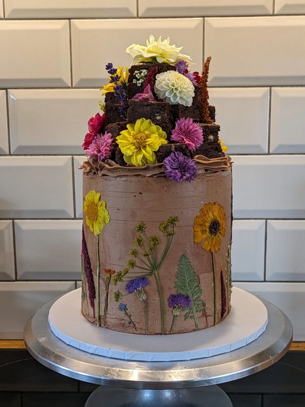 Chocolate cake with a brownie stack on top. Decorated with pressed and fresh edible flowers