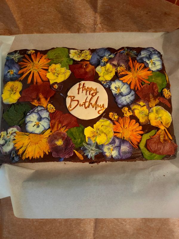 Chocolate brownie decorated with pressed edible flowers and 'happy birthday' written on