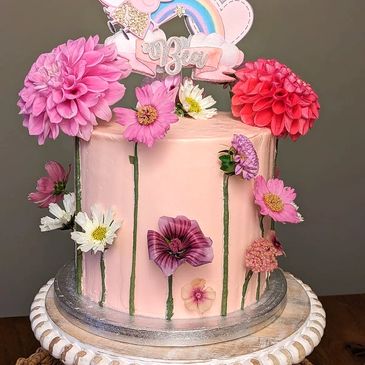 A pink cake decorated with fresh flower stems around the edge