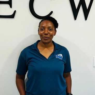Woman in a blue polo shirt standing against a white wall with black letters.