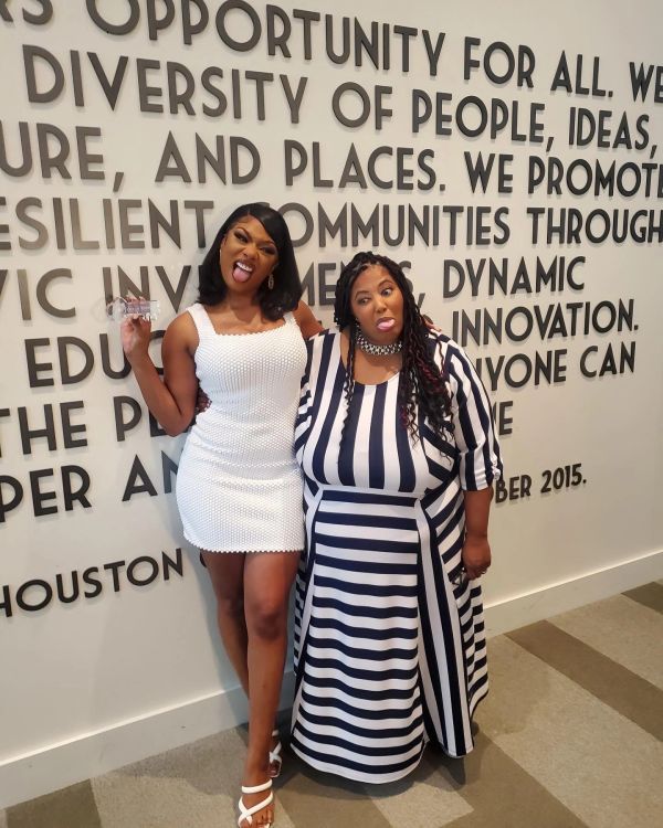 Two women making funny faces in front of a motivational wall with bold text.
