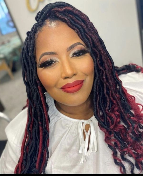 Smiling woman with long black and red braided hair and bold makeup.