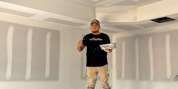Man giving thumbs up inside a newly drywalled room.