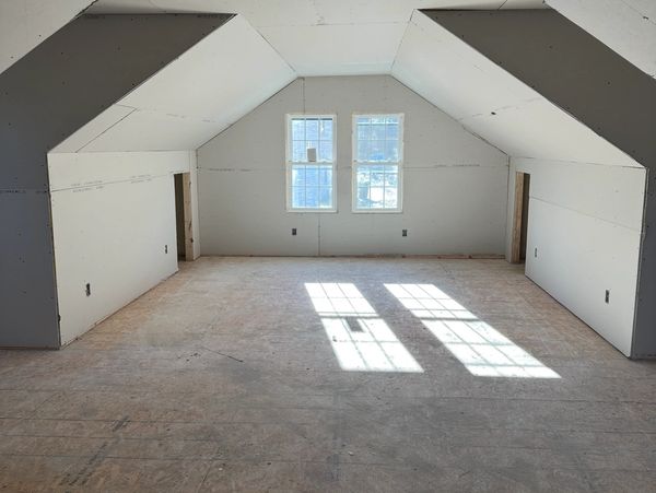 Empty attic space with drywall and two windows letting in sunlight.