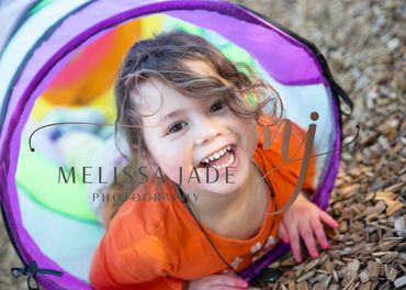 Smiling child playing inside a colorful tunnel at a playground.