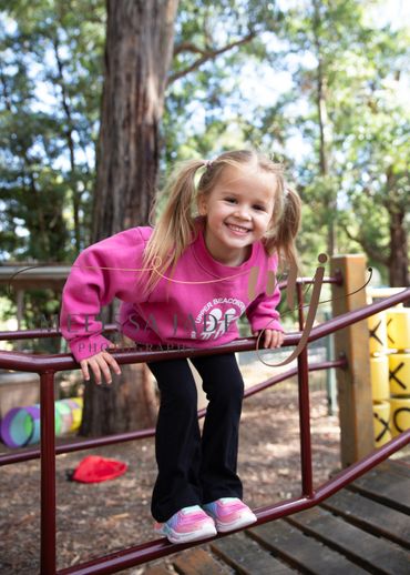 A young girl in a pink sweatshirt playing on playground equipment outdoors.