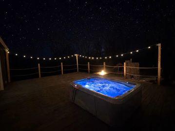 A glowing hot tub on a wooden deck under a starry night sky.