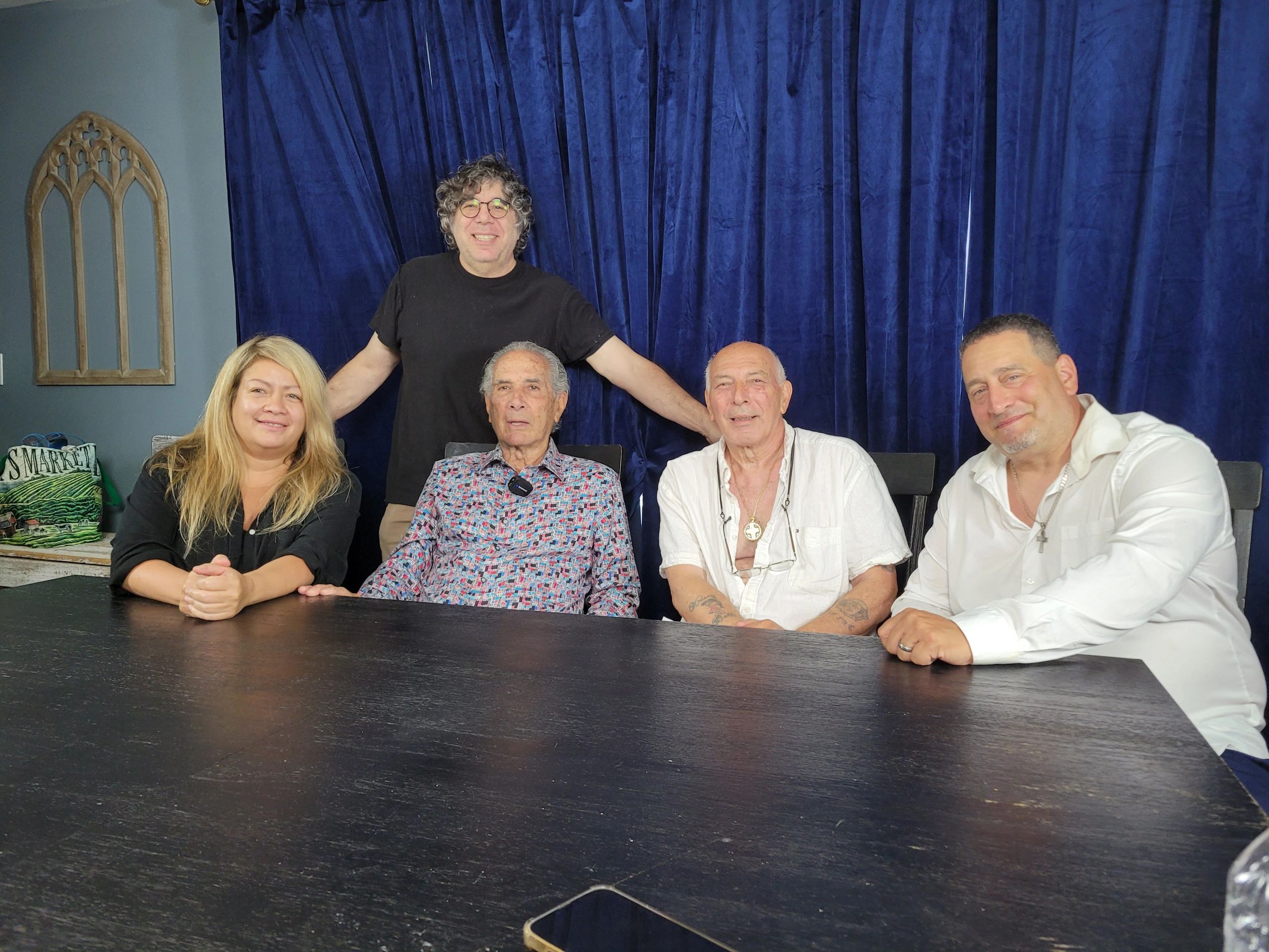 A four people sit on the chair and one guy stand out with looking on the camera