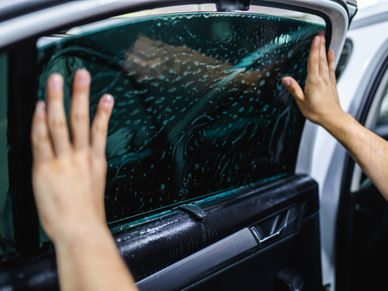 Person installing tinted film on a car window.