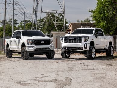 Two lifted white pickup trucks parked side by side outdoors.