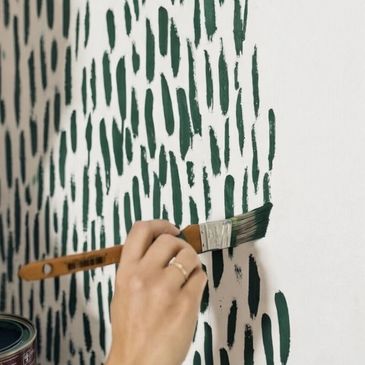 Hand painting green brushstroke pattern on white wall.