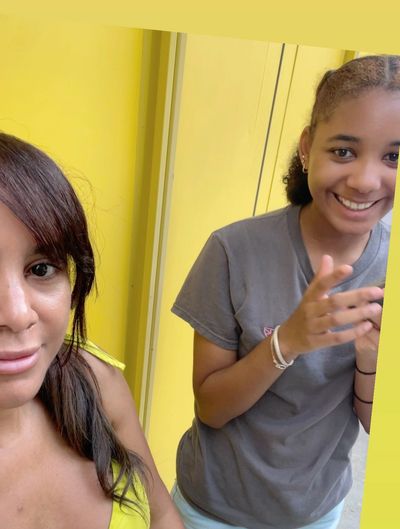 Karmel Graham, founder of SEE Computing, and her daughter standing in front of a yellow wall and smiling into the camera.