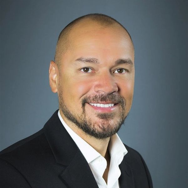 Smiling man with a beard in a black suit jacket.