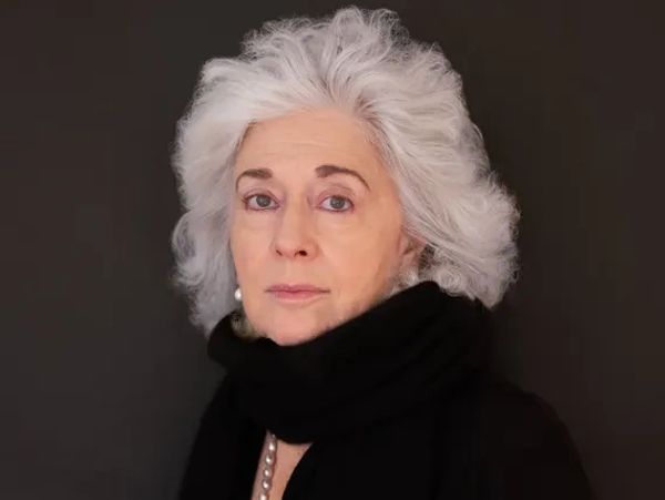 Elderly woman with white hair wearing a black scarf and pearl earrings.