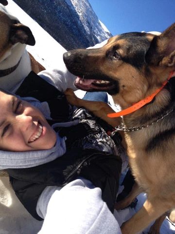 Person smiling with a German Shepherd in snowy mountains.