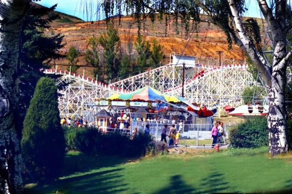 A lively amusement park with a roller coaster and colorful rides surrounded by trees and hills.