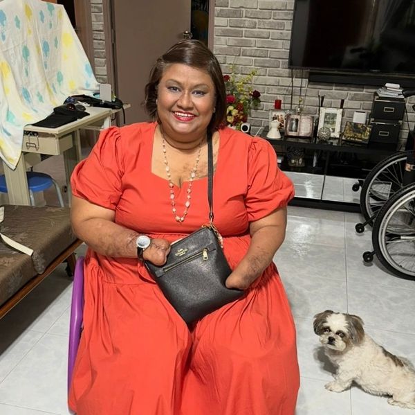 Carole in an orange dress with a long pearl necklace and a black sling back across her body. 