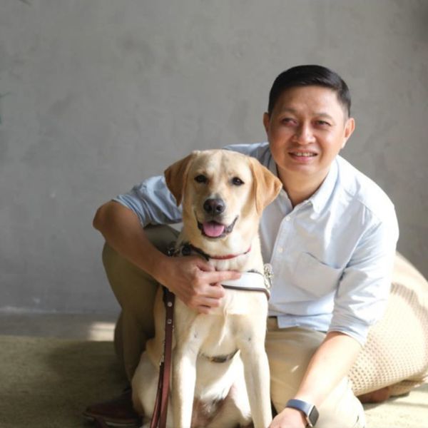 Sebastian sitting on the floor with his Labrador guide dog, Vogue. Light is coming from the right