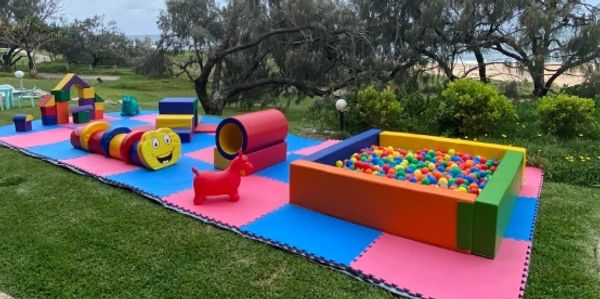 Outdoor children's play area with colorful mats, toys, and a ball pit.