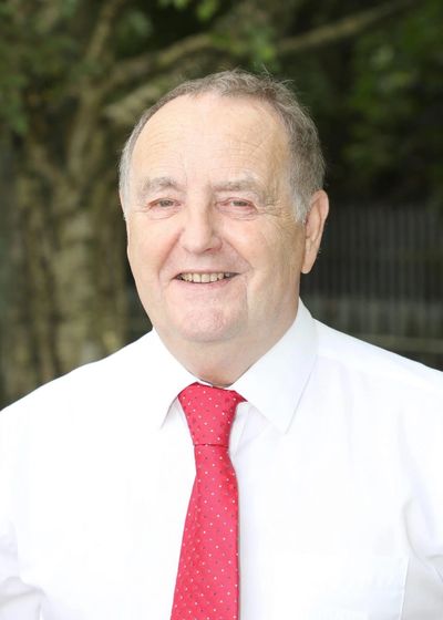 Smiling elderly man outdoors in white shirt and red tie.