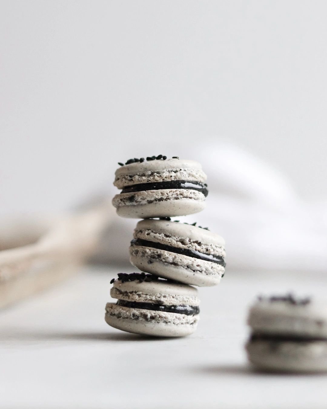 three black sesame macarons precariously stacked on top of each other in front of a baking tray.