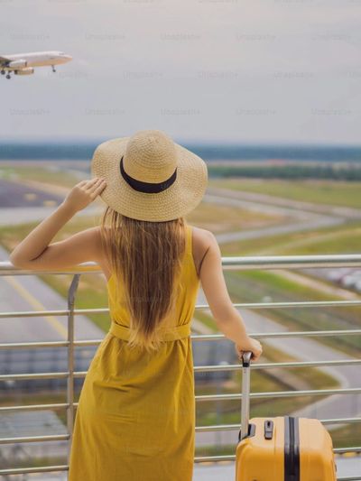 A woman in a yellow dress watching an airplane at the airport.