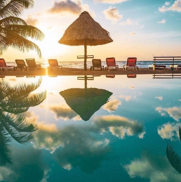 Sunset at a beachside pool with palm trees and lounge chairs.